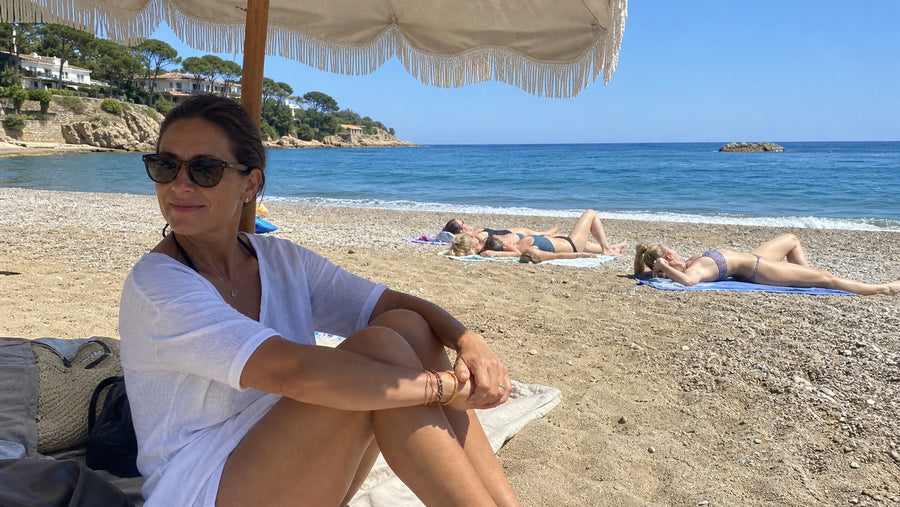 Bronzed woman sitting beneath a beach parasol while friends sunbathe nearby